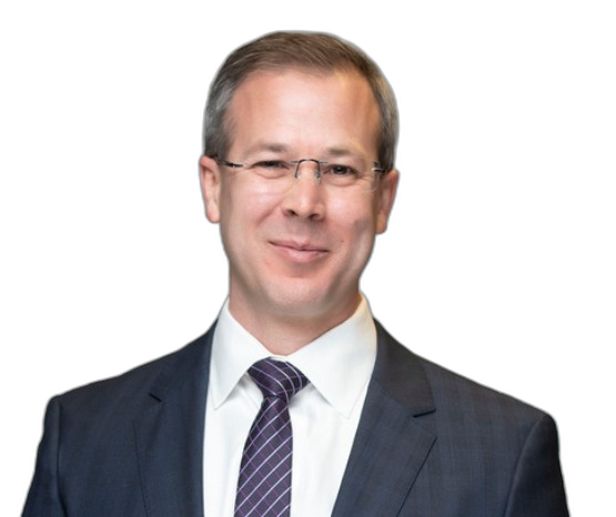 Jesse J. Camacho, in a navy suit and glasses, smiling toward the camera.